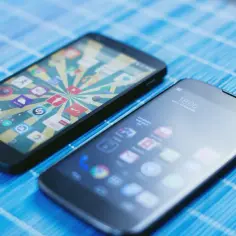 Dwa smartfony z ikonami aplikacji na ekranach, leżące na niebieskiej macie.